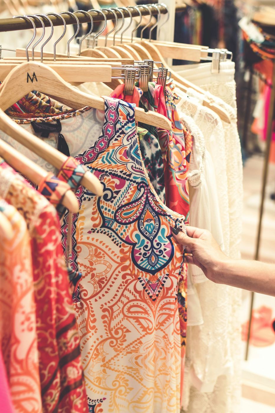 Hand selecting a printed dress from a clothing rack